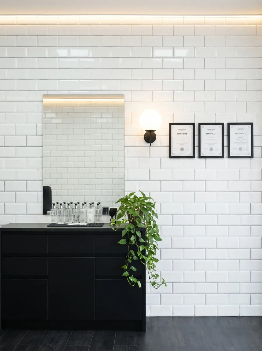Estación de trabajo en Barbelogía: espejo, mueble negro y azulejo blanco biselado.